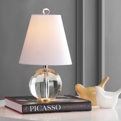 a table with a lamp, book and bird figurine on top of it