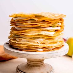 a stack of pancakes sitting on top of a white cake plate next to an apple