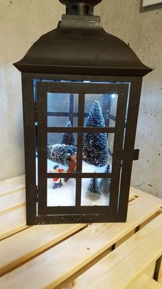 a lantern is sitting on top of a wooden table with snow around it and trees in the window