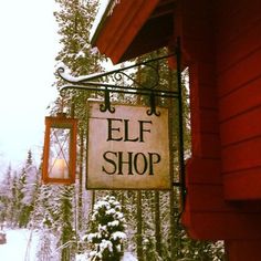 a sign hanging from the side of a red building next to a snow covered forest