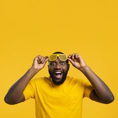 a man in yellow shirt holding up sunglasses over his eyes with both hands on top of his head