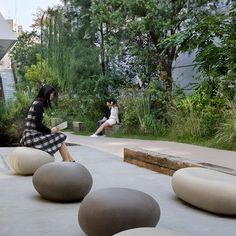 two people sitting on large rocks in the middle of a courtyard area with trees and bushes