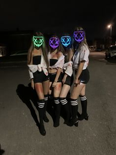 three girls wearing neon masks standing in the middle of a parking lot at night with their arms around each other