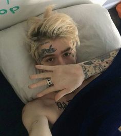 a man with tattoos on his arm laying in bed next to a pillow and pillows