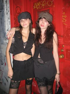 two women standing next to each other in front of a red door