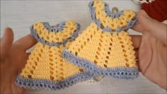 two crocheted yellow and blue outfits being held by someone