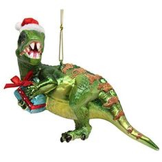 Blown glass green dinosaur ornament holding a blue and red gift, wearing a Santa hat. Glass Dinosaur, Weird Ornaments, Tree Dazzler, Dinosaur Christmas Ornament, Dinosaur Christmas Tree, Dinosaur Ornament, Glass Theme, Holiday Snowflakes, Christmas Material