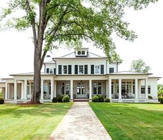 a large white house sitting on the side of a lush green field next to a tree