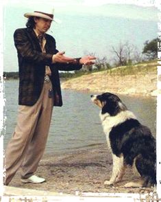 a man standing next to a black and white dog on a beach near the water