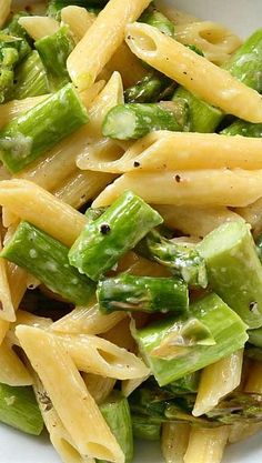 a white bowl filled with pasta and asparagus on top of a wooden table