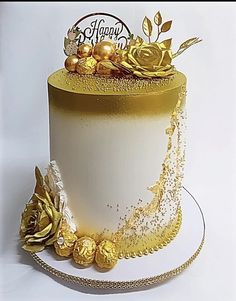 a white and gold decorated cake with flowers on the top is sitting on a plate