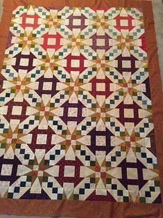 a quilt is laying on the floor in front of a tablecloth with an orange border