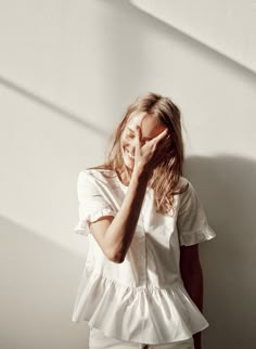 a woman standing in front of a white wall holding her hands to her face and smiling