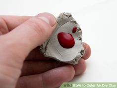 a hand holding a small piece of clay with red hearts on it's face