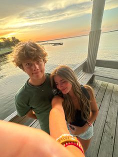 two young people taking a selfie on a pier at sunset with the sun setting in the background