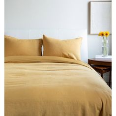 a bed with yellow sheets and pillows in a white room next to a wooden table