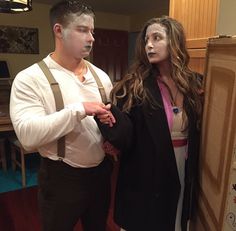 a man and woman standing next to each other in a room with wooden floors, wearing suspenders