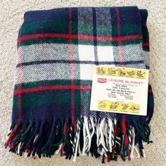 a green, white and red plaid blanket sitting on the floor next to a tag