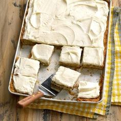 a pan filled with white frosted cake next to a yellow checkered napkin and knife