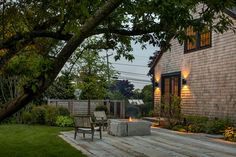 an outdoor fire pit in the middle of a yard with two chairs and a table next to it