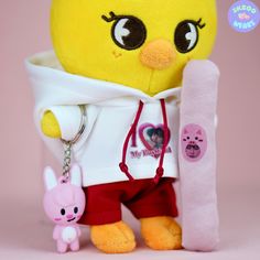 a yellow stuffed animal holding onto a pink keychain with an emo chick on it's back