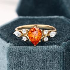 an orange heart shaped diamond ring sitting on top of a gray box with white diamonds