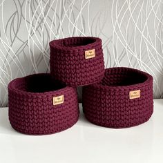 three knitted baskets sitting on top of a white table next to a wallpaper