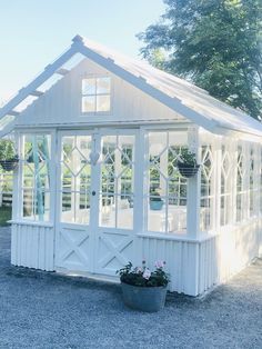 a small white house sitting on top of a gravel lot next to a tree and bushes