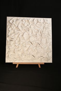 a white sculpture sitting on top of a wooden easel in front of a black background