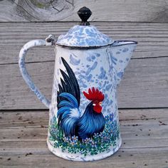 a blue and white pitcher with a rooster painted on it's side sitting on a wooden surface