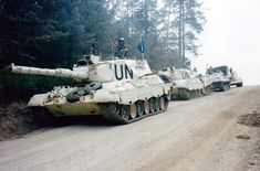 tanks are lined up on the side of a dirt road in front of some trees