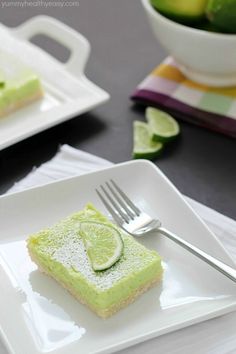 a slice of lime cake on a plate with a fork and bowl of limes in the background