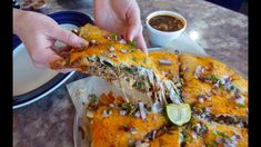 a person reaching for a piece of mexican food on a plate with dipping sauces