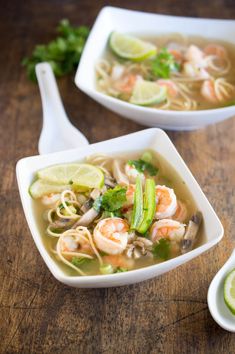 two white bowls filled with shrimp and noodle soup on top of a wooden table