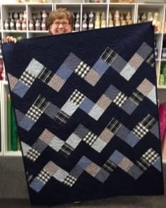 a woman holding up a quilt in front of a book shelf