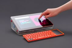 an orange keyboard sitting on top of a laptop computer next to a hand holding a mouse