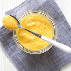 a glass jar filled with yellow liquid on top of a blue napkin next to a spoon