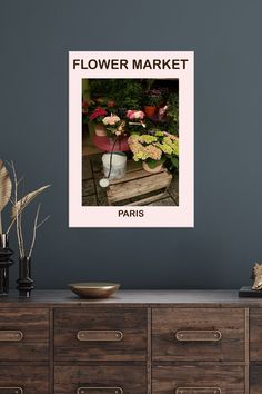 a flower market poster hanging on the wall next to a dresser with vases and flowers