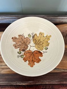 a plate with leaves painted on it sitting on top of a wooden table next to a window