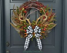 a wreath with deer antlers and plaid bow hangs on the front door's black door