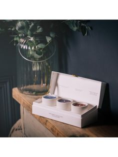 two cups in a box sitting on a table next to a vase filled with flowers