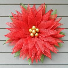 a red and green wreath with three gold balls on it's center, hanging from the side of a house