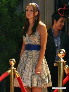 a woman in a dress standing next to a red carpet and barrier with two men behind her