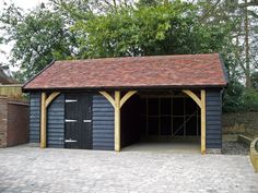 a black garage with a red roof and brick pavers flooring in front of it