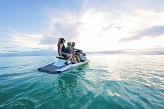 three people on a jet ski in the ocean at sunset or sunrise, with one person sitting