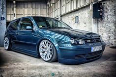 a blue car parked in front of a brick wall with graffiti written on it's side