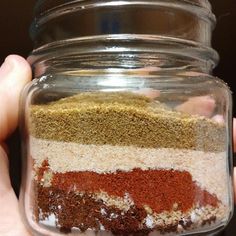 a person holding up a jar filled with different colored seasoning in it's hands