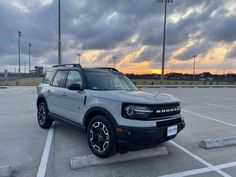 an suv parked in a parking lot with the sun setting behind it and dark clouds