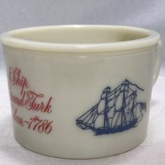 a white bowl with a blue and red ship on the front is sitting on a table