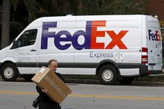 a fed ex delivery truck driving down the street with a man carrying a box on his back